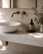 A modern bathroom vanity setup with a white marble vessel sink, matching marble countertop, matte brass wall-mounted faucet and controls.